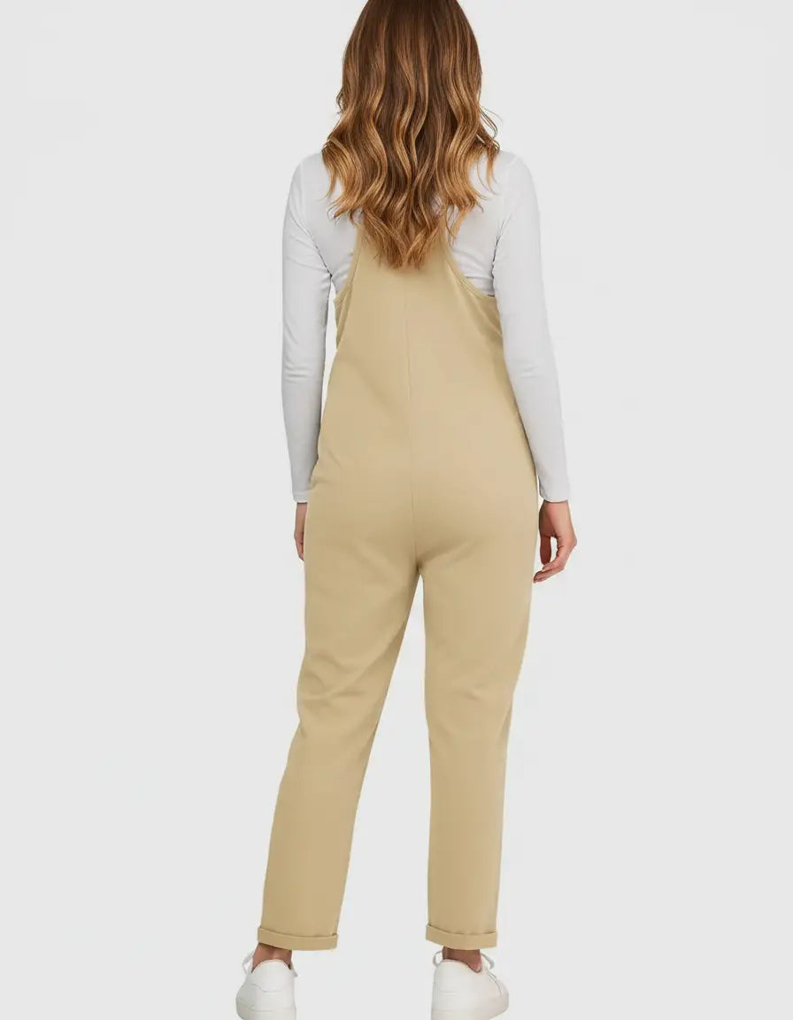 Woman from behind wearing a beige adjustable strap maternity jumpsuit over a white long-sleeve top.