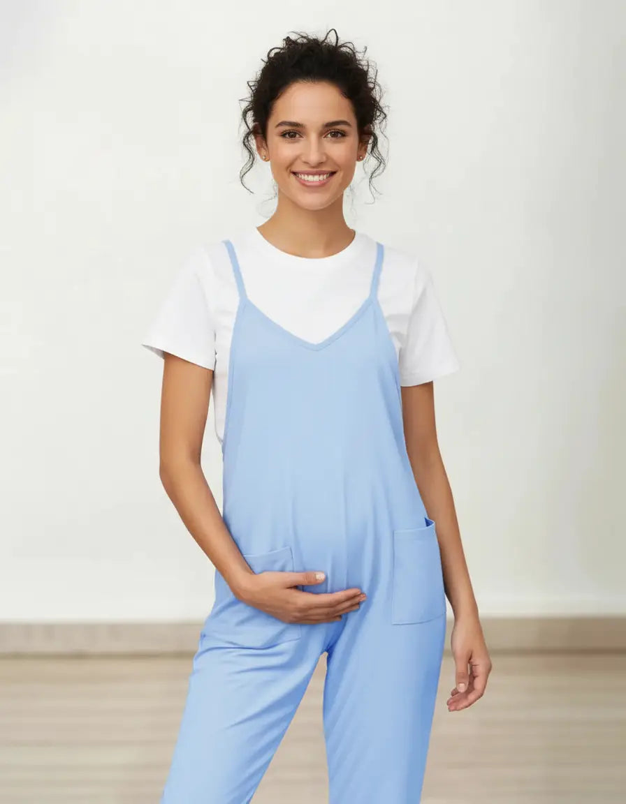Smiling pregnant woman in a light blue flowy maternity jumpsuit with adjustable straps and pockets.