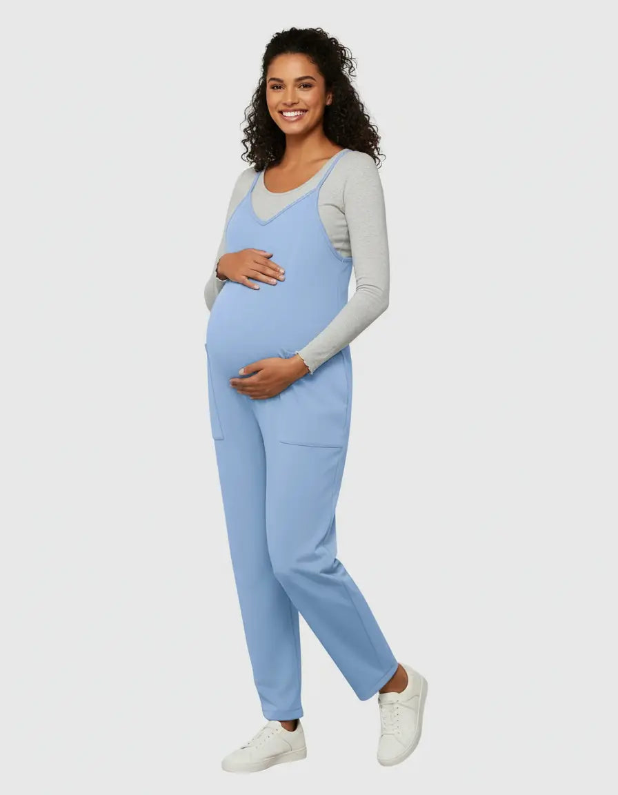Smiling pregnant woman in a light blue flowy maternity jumpsuit with adjustable straps and pockets.