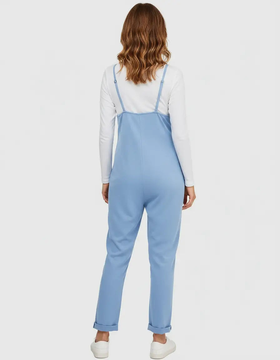 Woman from behind wearing a light blue flowy maternity jumpsuit with adjustable straps over a white long-sleeve shirt.