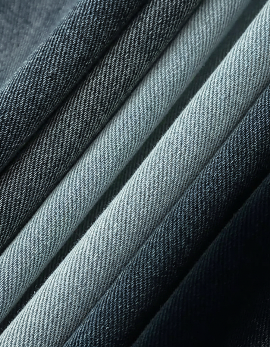 Close-up of folded denim fabric in varying shades of blue and gray, showcasing texture.