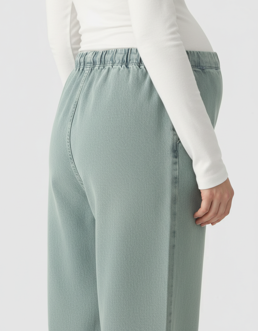 Pregnant woman wearing light green wide-leg maternity denim pants with an adjustable elastic waist.