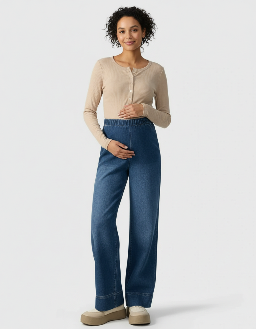 Smiling pregnant woman in beige ribbed long-sleeve top and blue wide-leg maternity denim pants.