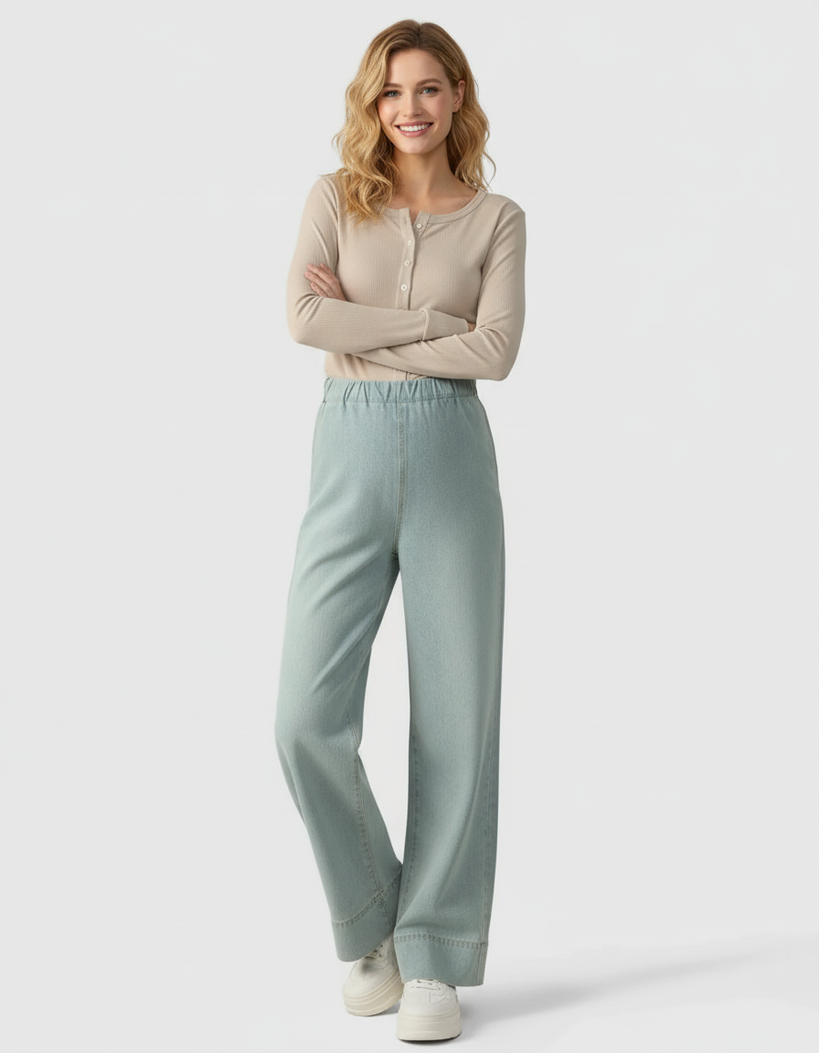 Smiling woman in light wash wide-leg maternity denim pants and a beige long-sleeve top.