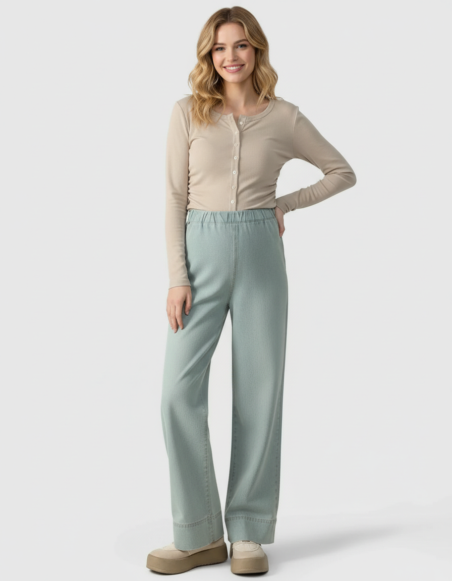 Smiling woman in beige long-sleeve top and light blue wide-leg maternity denim pants.