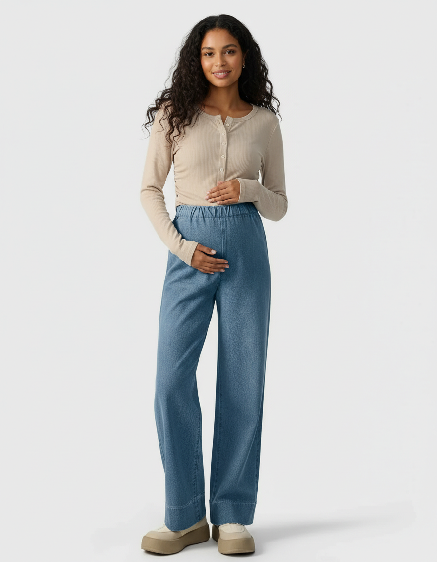 Smiling pregnant woman in light wash wide-leg maternity denim pants and a beige ribbed top.