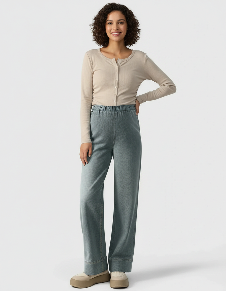 Smiling woman in beige long-sleeve top and light blue wide-leg maternity denim pants.