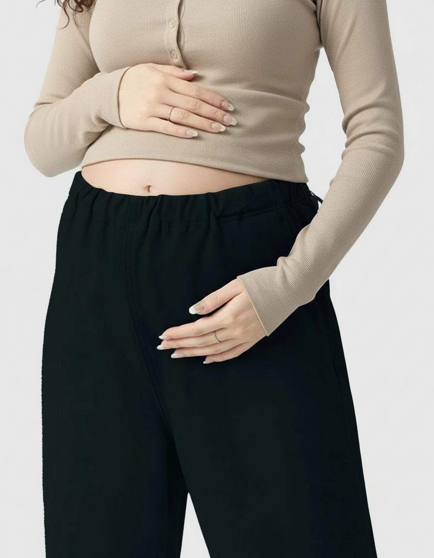 Pregnant woman in black wide-leg maternity denim pants with an adjustable waist and a beige ribbed top.
