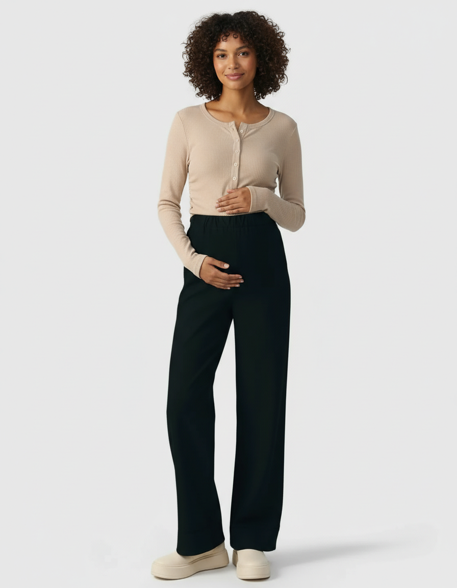 Smiling pregnant woman in a beige ribbed long-sleeve top and black wide-leg maternity pants.