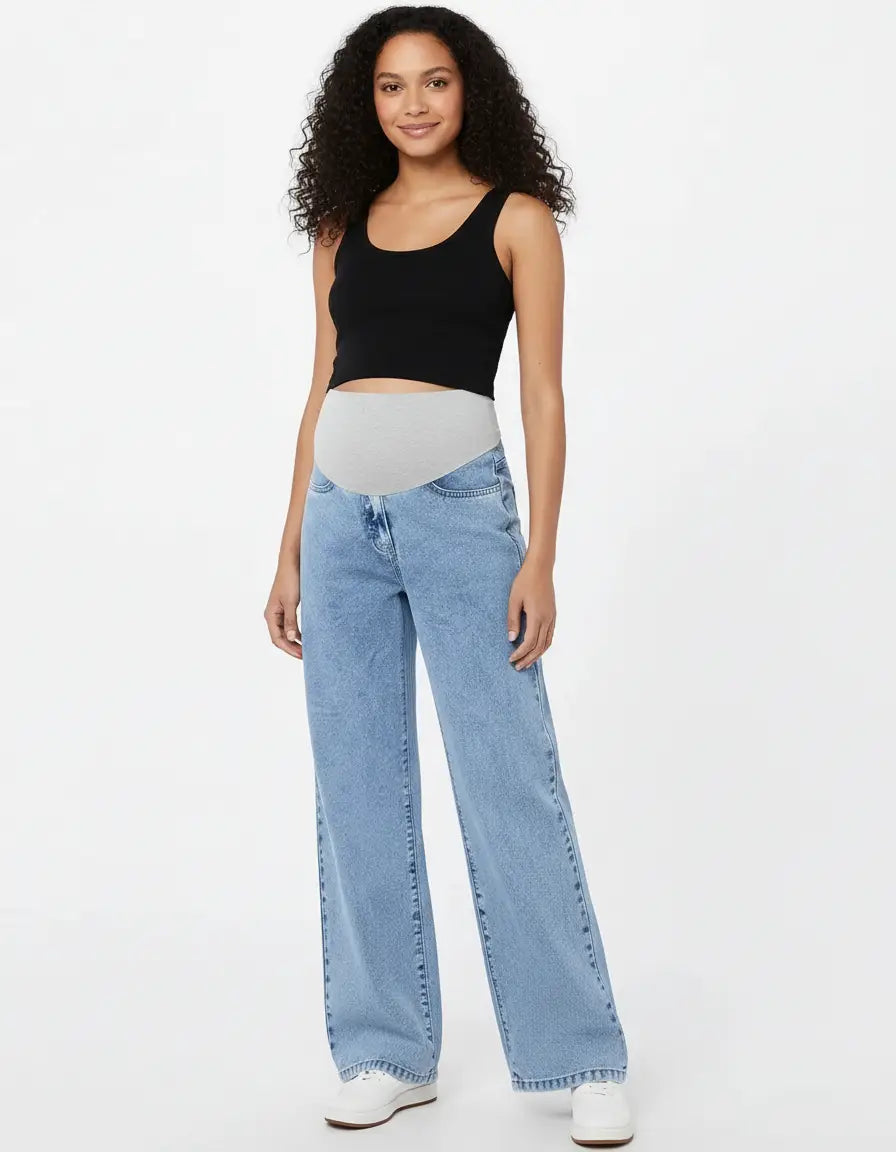 Smiling pregnant woman in light wash wide-leg maternity jeans with a grey adjustable waistband and a black tank top.