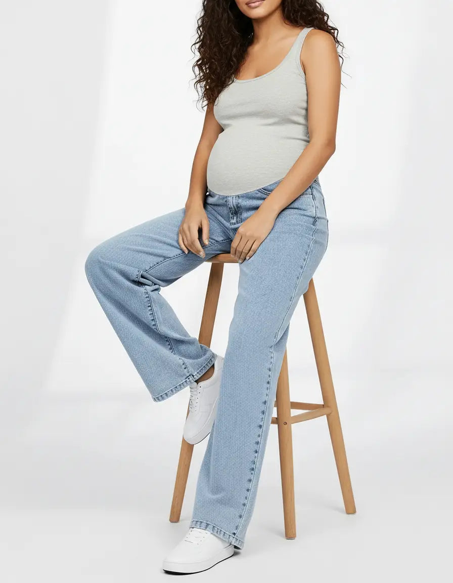 Pregnant woman in light wash wide-leg maternity jeans with an adjustable waistband and a grey tank top.