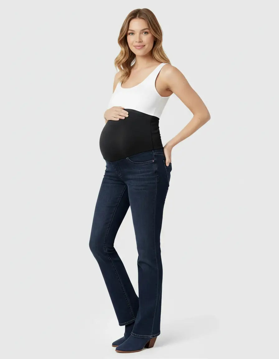 Smiling pregnant woman in dark wash, flared-leg maternity jeans with a black over-belly panel and white tank top.