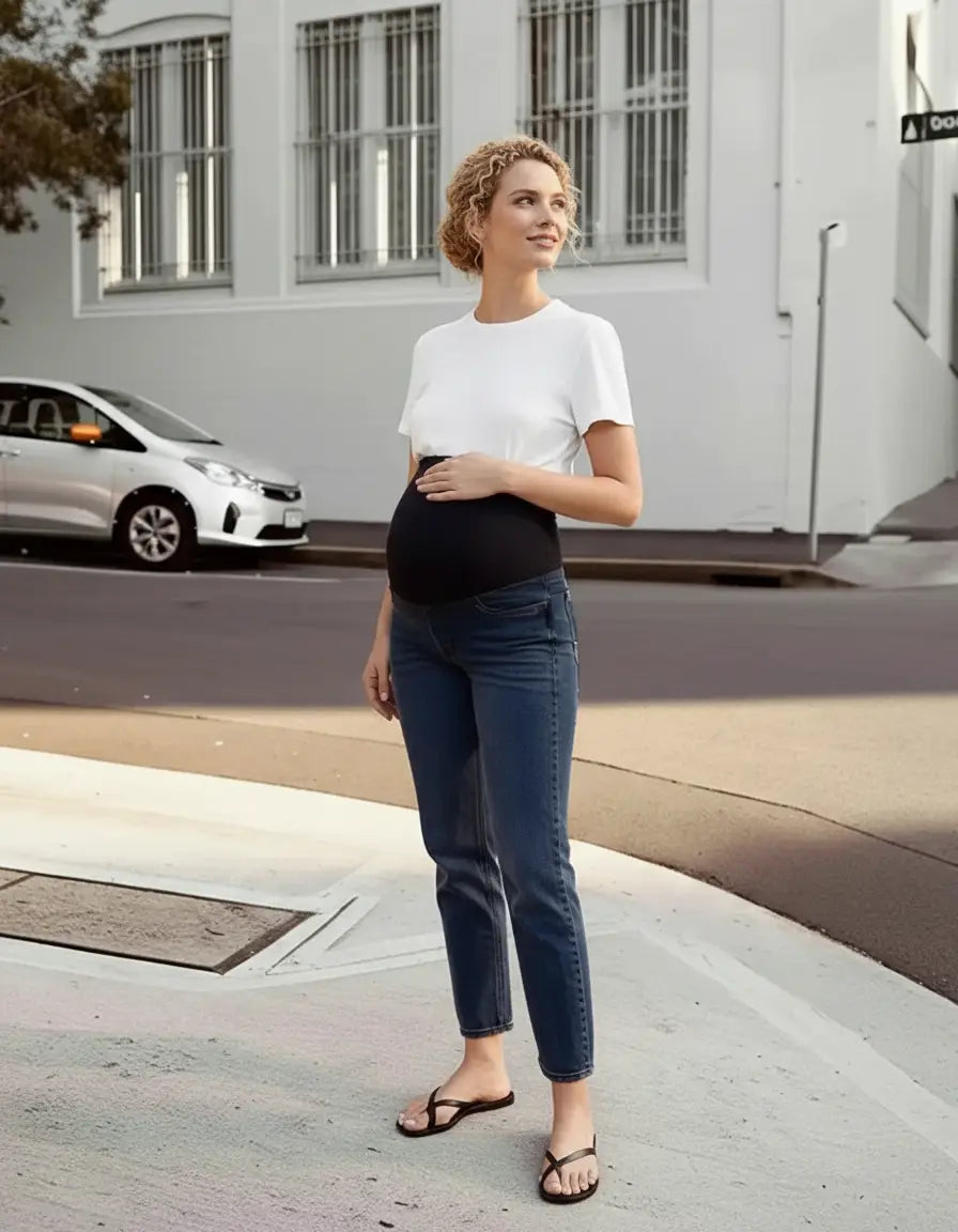 Pregnant woman in classic blue high-waist flared maternity jeans with a black over-belly panel and white t-shirt.