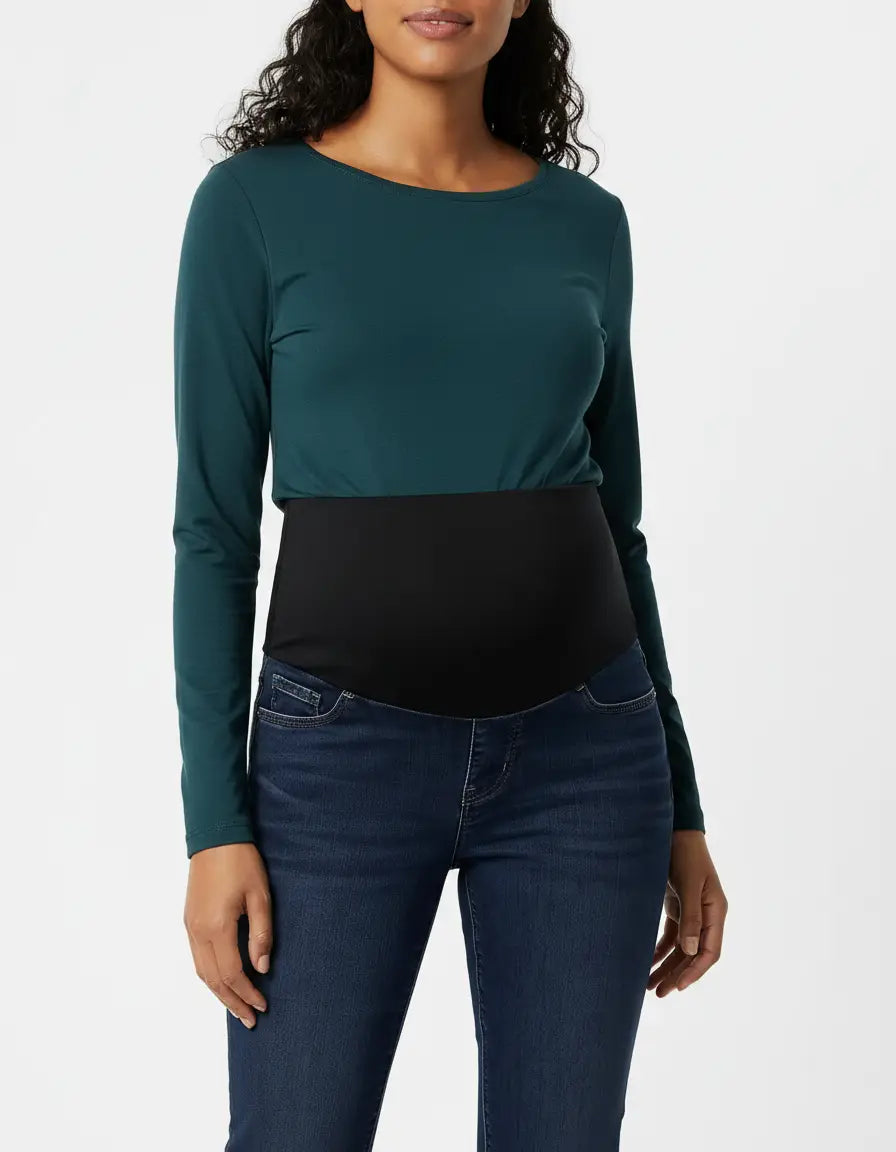 Woman wearing dark wash, high-waist flared-leg maternity jeans with a black over-belly panel and a teal long-sleeve top.