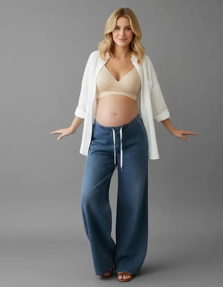 Pregnant woman in blue wide-leg maternity jeans with a drawstring waist, beige bra, and white shirt.
