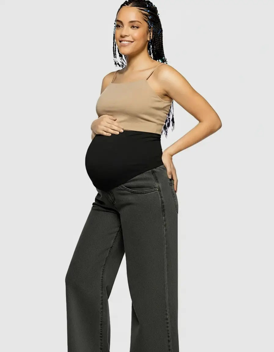 Smiling pregnant woman in a beige tank top and dark gray wide-leg maternity jeans with a black elastic waist.