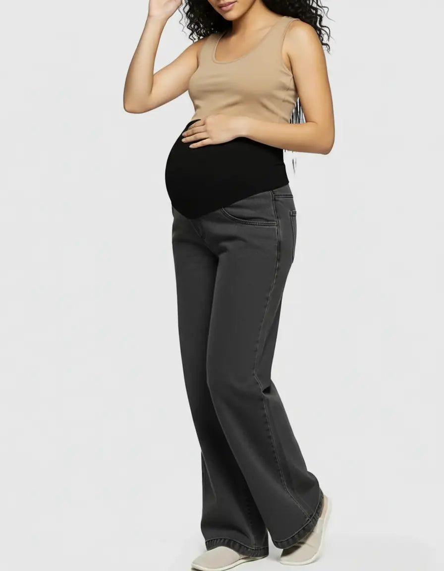 Maternity jeans with a black elastic waist and wide-leg dark gray denim, paired with a beige tank top.