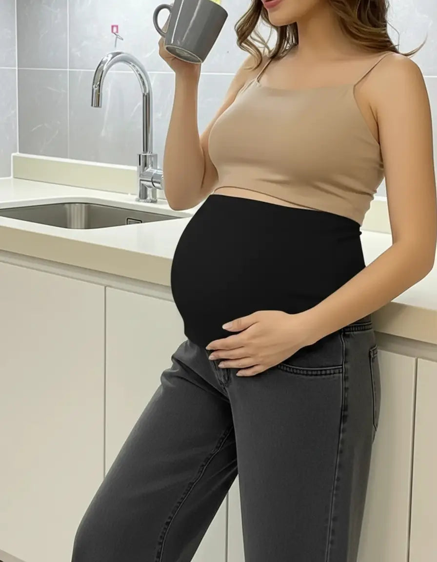 Pregnant woman in black wide-leg maternity jeans with an elastic waist and a beige tank top, holding a mug.