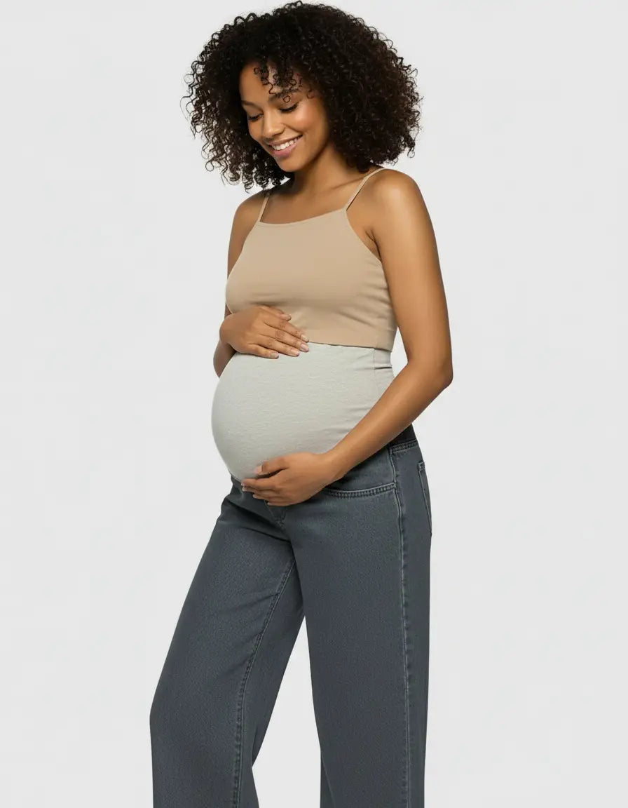 Smiling pregnant woman in a beige tank top and grey wide-leg maternity jeans with a light grey elastic waist.