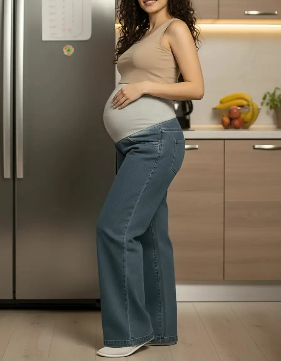 Pregnant woman in a beige tank top and blue wide-leg maternity jeans with a grey elastic waist.