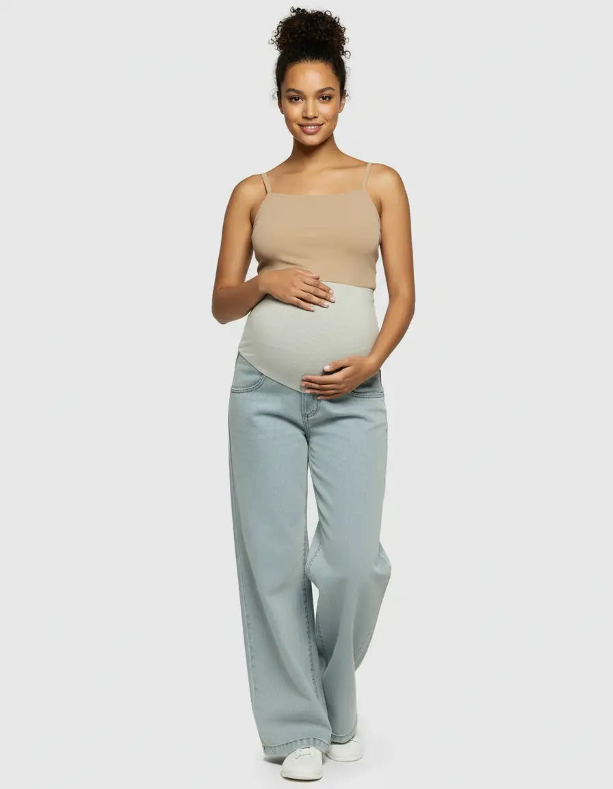Smiling pregnant woman in light wash wide-leg maternity jeans with a light gray elastic waist and a beige tank top.
