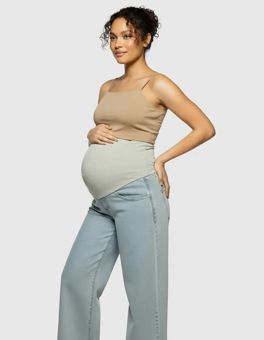 Pregnant woman in light wash wide-leg maternity jeans with a grey elastic waist and a beige tank top.