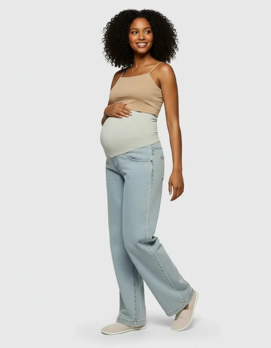 Smiling pregnant woman in light wash wide-leg maternity jeans with an elastic waist and a beige tank top.