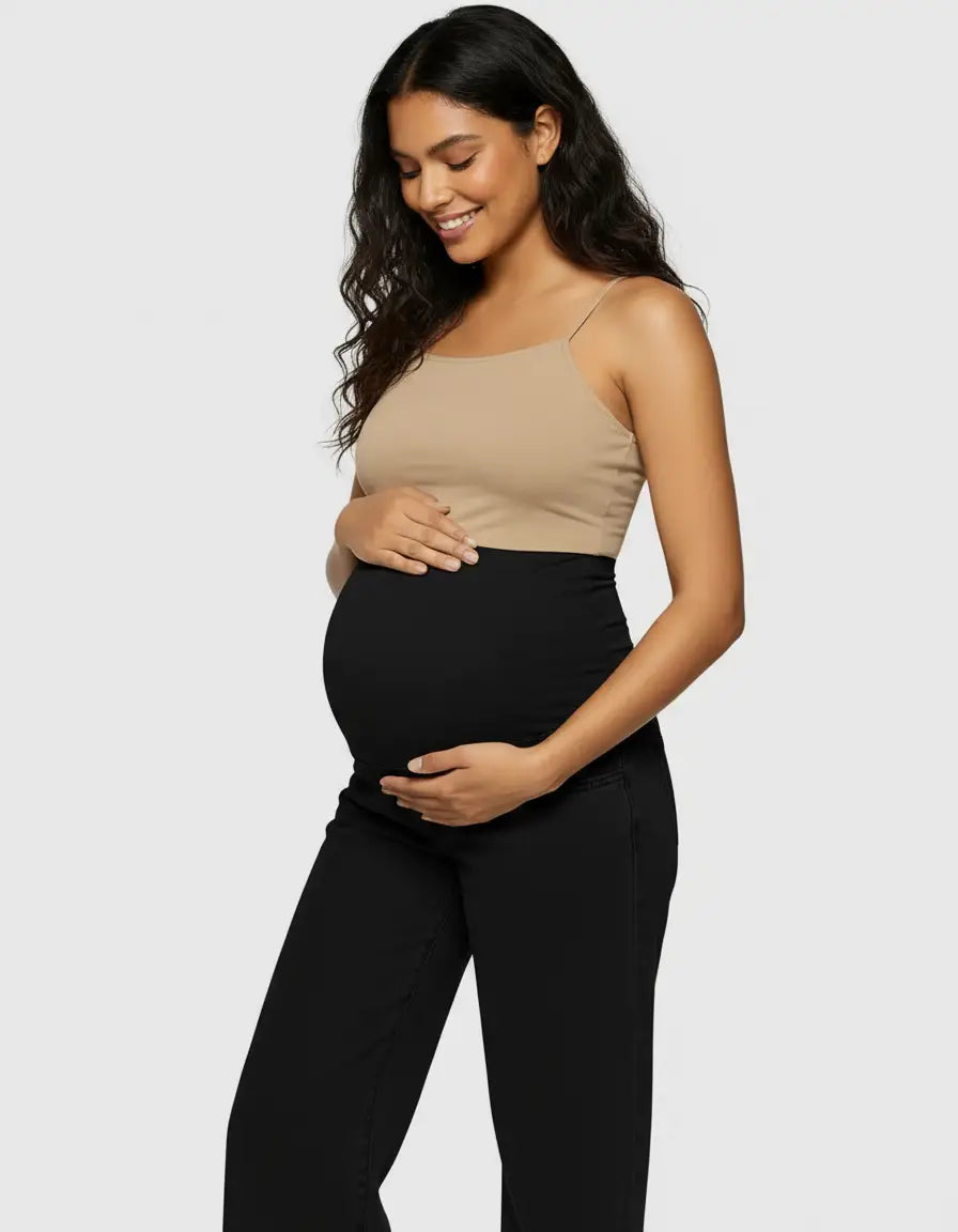 Smiling pregnant woman in black wide-leg maternity jeans with an elastic waist and a beige camisole.
