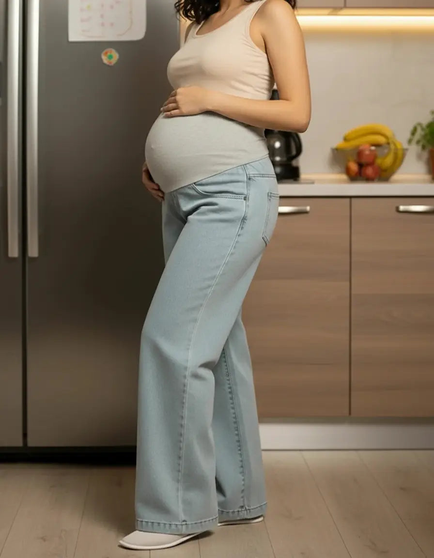 Pregnant woman in light wash wide-leg maternity jeans with a comfortable elastic waist and a beige tank top.