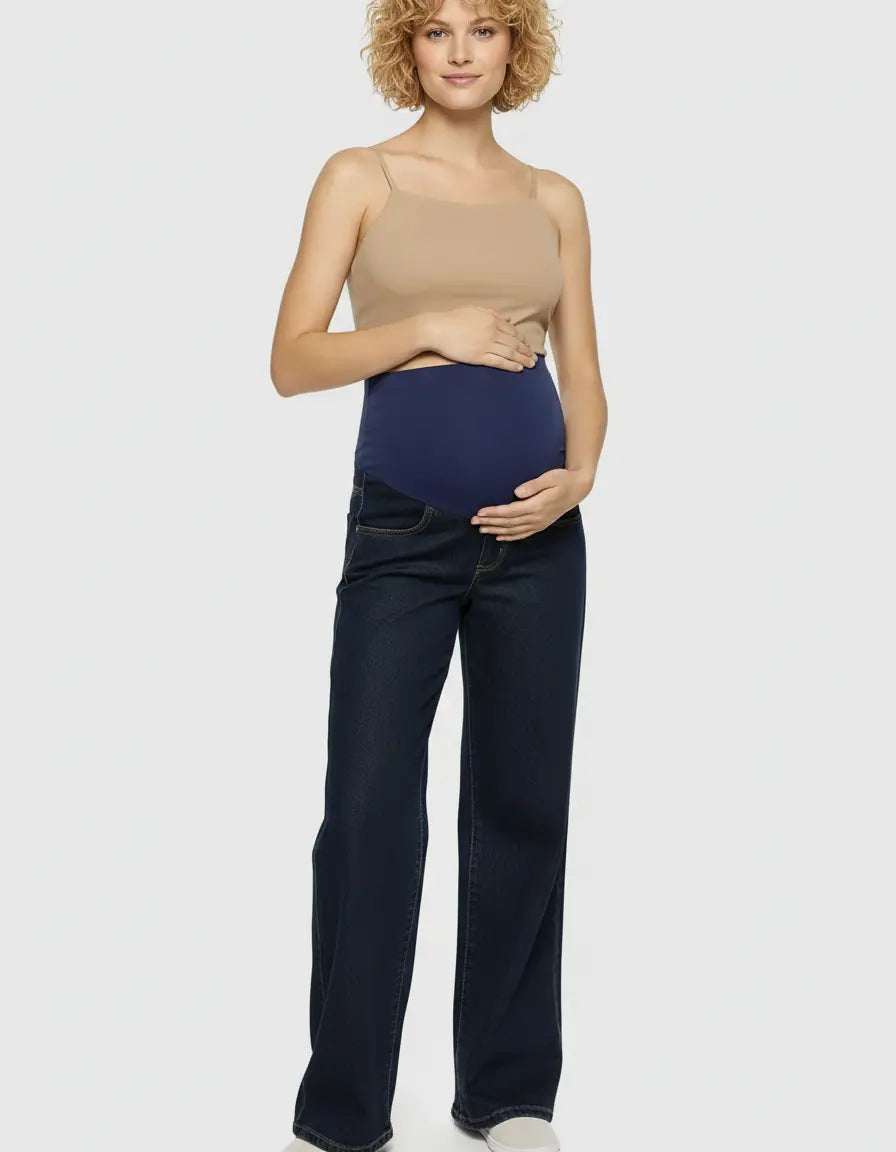Pregnant woman in dark wash wide-leg maternity jeans with a navy elastic waist and a beige tank top.