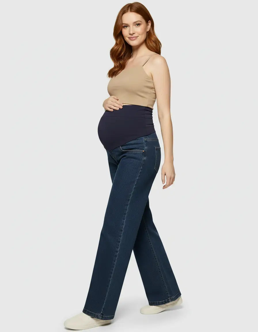Pregnant woman in dark wash wide-leg maternity jeans with a navy elastic waist panel and a beige tank top.