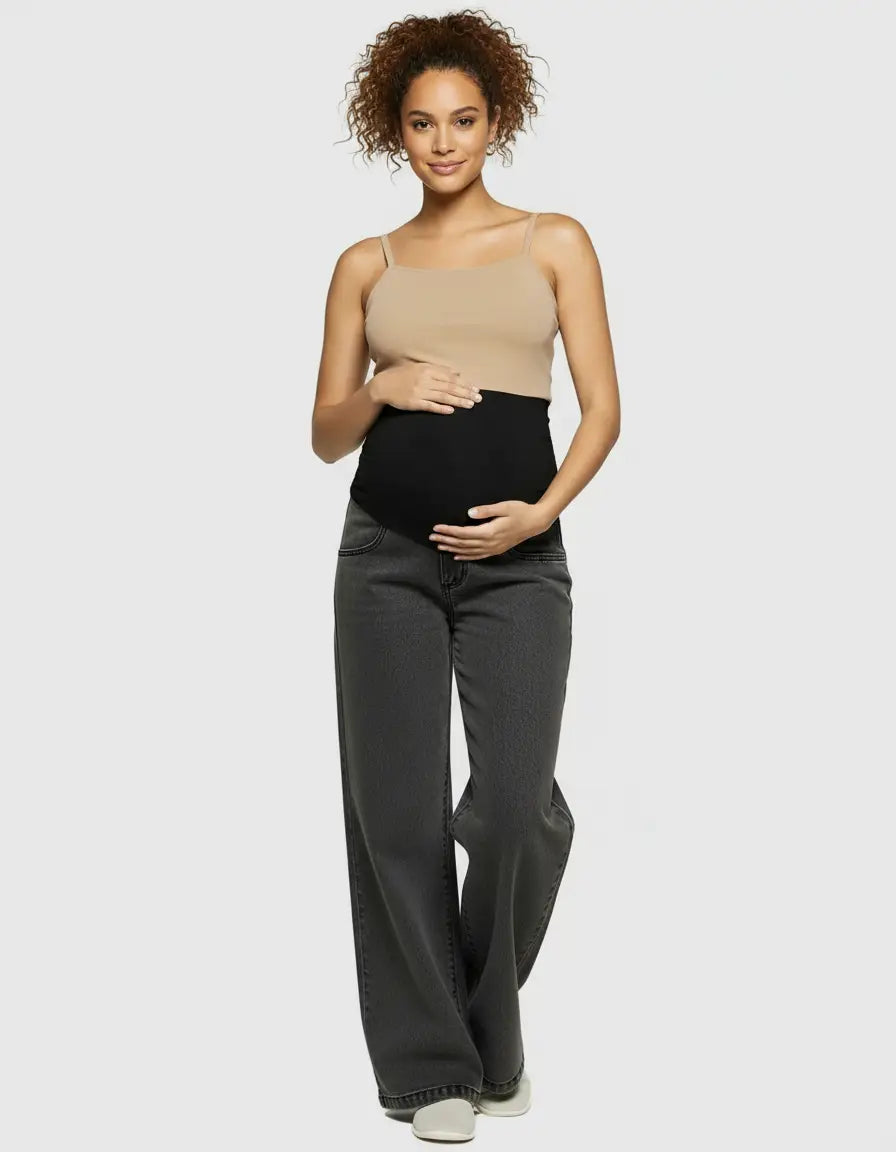 Smiling pregnant woman in a beige tank top and black elastic waist wide-leg maternity jeans.