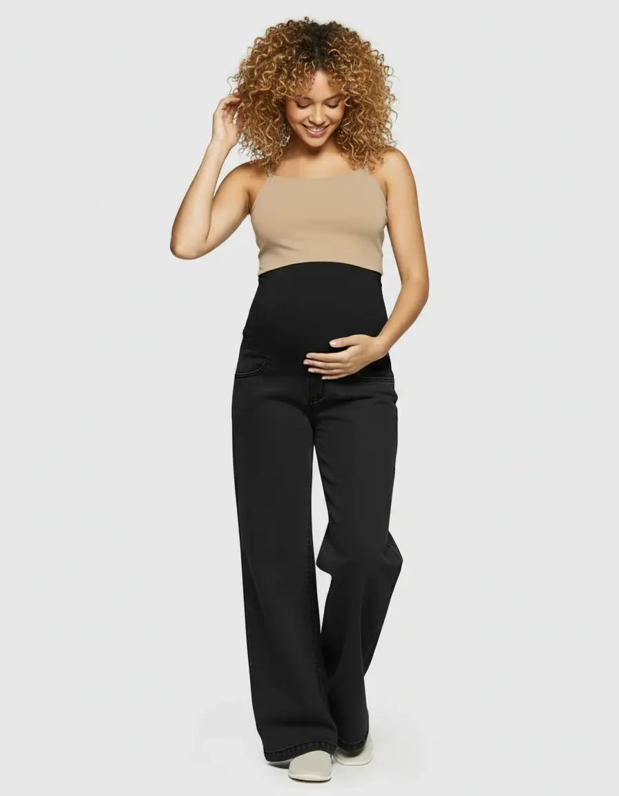 Smiling pregnant woman in black wide-leg maternity jeans with elastic waist and a beige top.