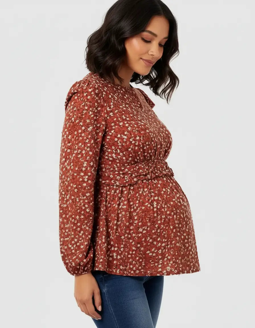 Maternity model wearing a rust floral print tie-waist top with long sleeves and a relaxed fit.