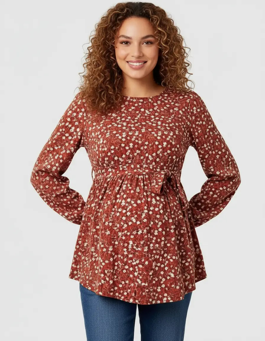 Smiling pregnant woman in a rust-colored floral print maternity top with a tie waist and long sleeves.