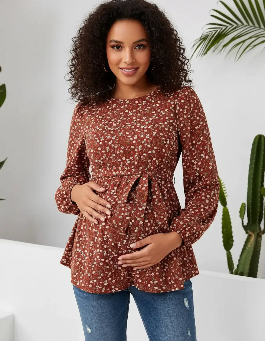 Smiling pregnant woman in a rust floral print tie-waist maternity top with long sleeves, holding her belly.