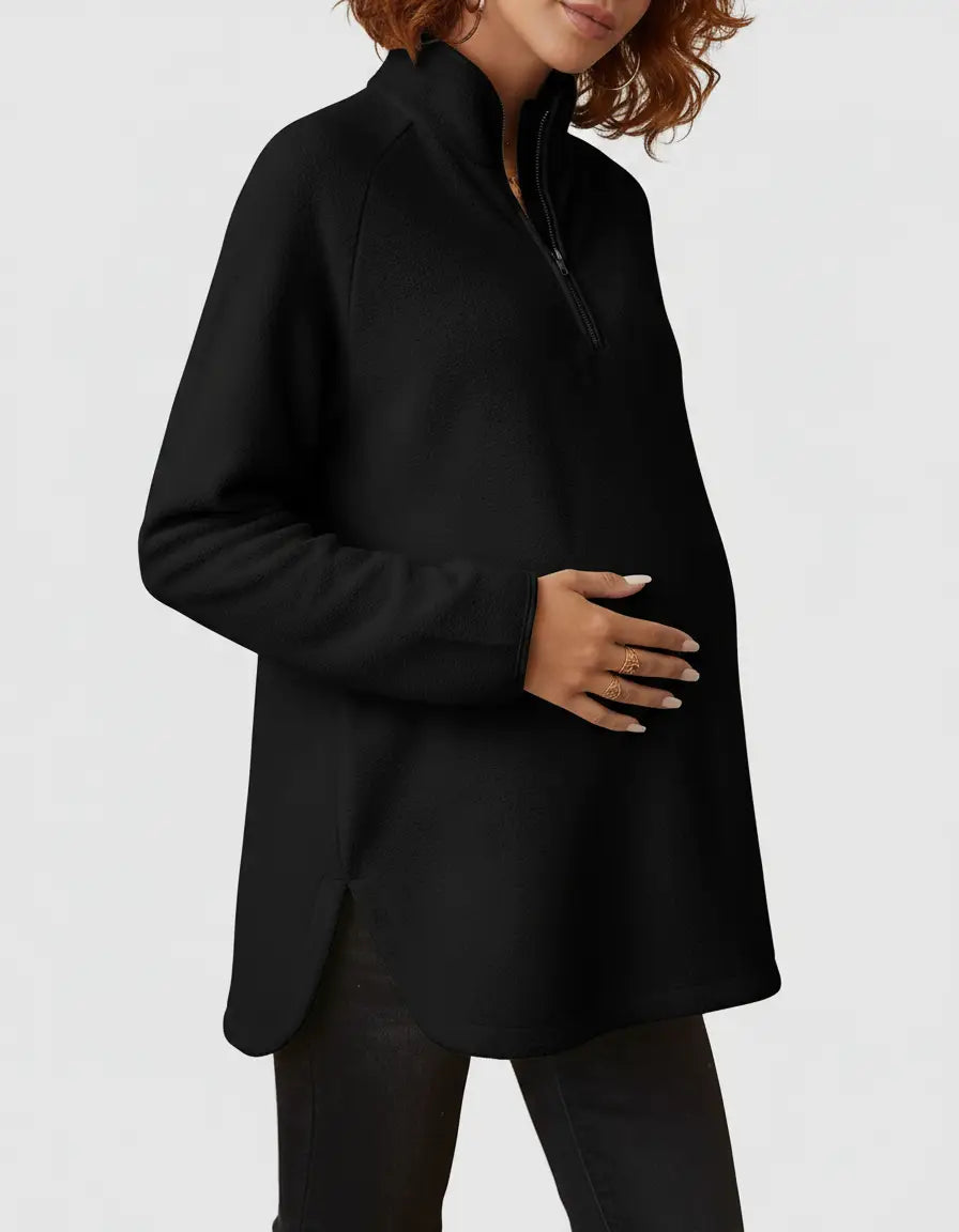 Black soft knit maternity half-zip long sleeve top with stand collar and side slits, worn by a pregnant woman.