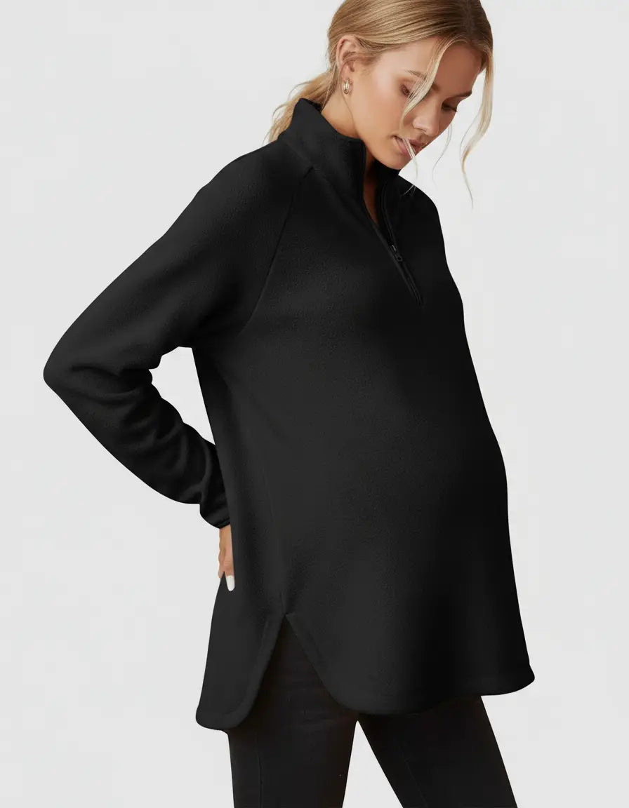 Pregnant woman wearing a black half-zip long sleeve maternity top with a stand collar and side slits.