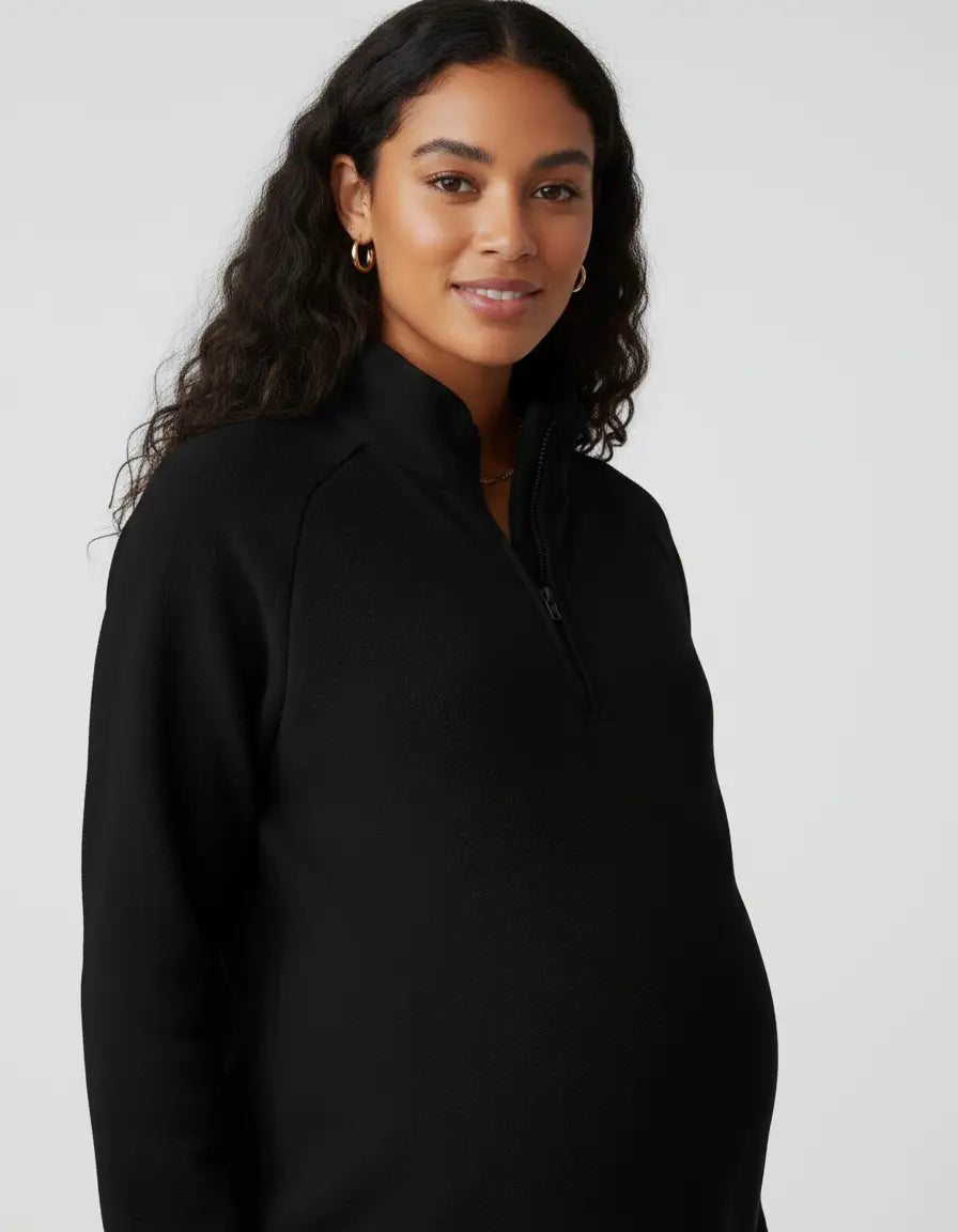 Smiling pregnant woman in a black soft knit half-zip long sleeve maternity top with a stand collar.