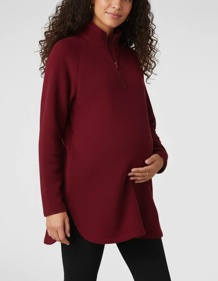 Maternity model in a relaxed-fit, burgundy half-zip long sleeve top with a stand collar and side slits.