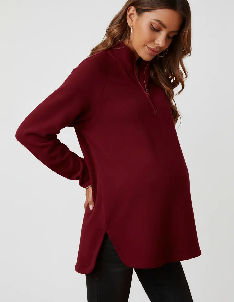 Pregnant woman in a relaxed-fit, burgundy half-zip long sleeve maternity top with side slits.