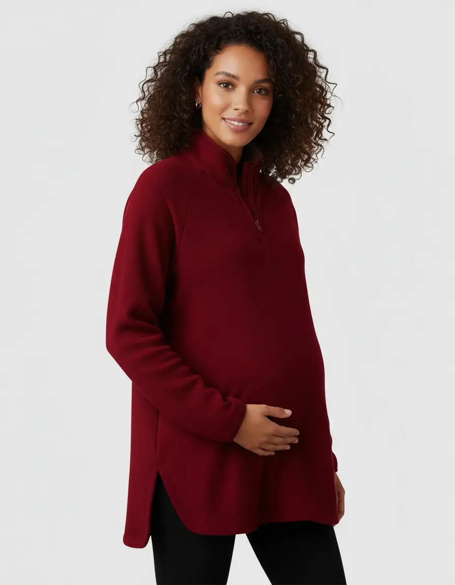 Smiling pregnant woman in a red half-zip long sleeve maternity top with side slits.