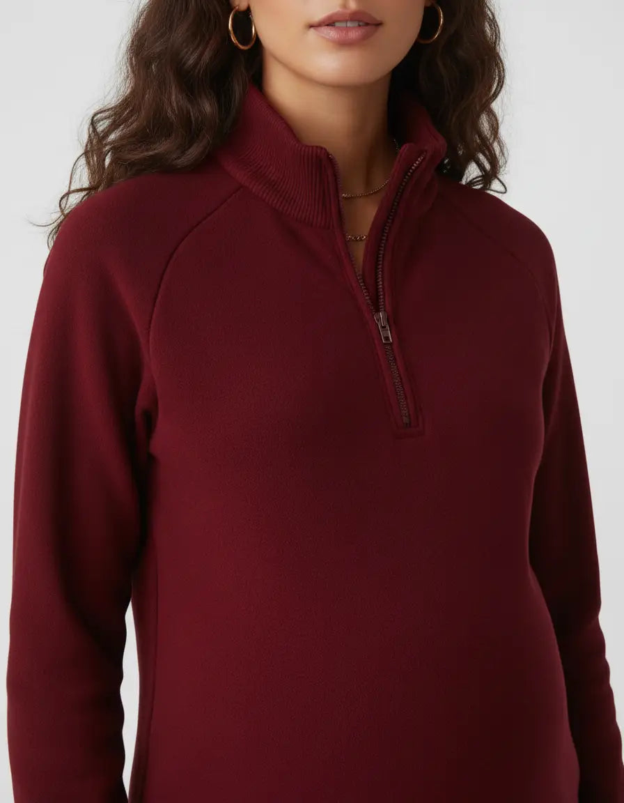 Woman wearing a burgundy soft knit half-zip long sleeve maternity top with a stand collar.