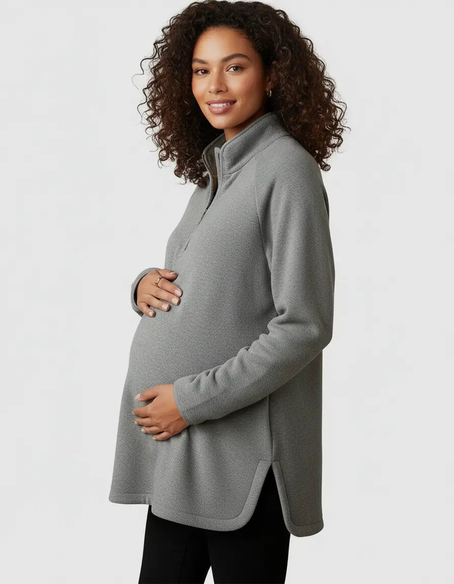 Smiling pregnant woman in a gray soft knit half-zip long sleeve maternity top with side slits.