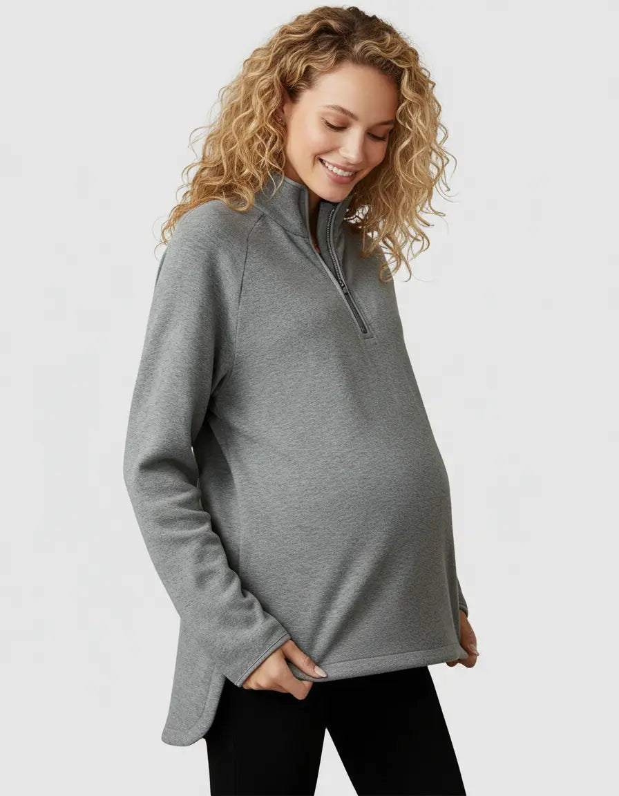 Smiling pregnant woman in a gray half-zip long sleeve maternity top with a relaxed fit and side slits.