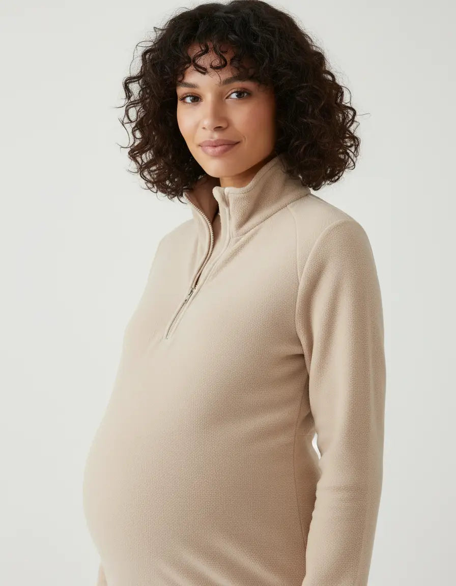 Pregnant woman wearing a beige half-zip long sleeve maternity top with a stand collar.