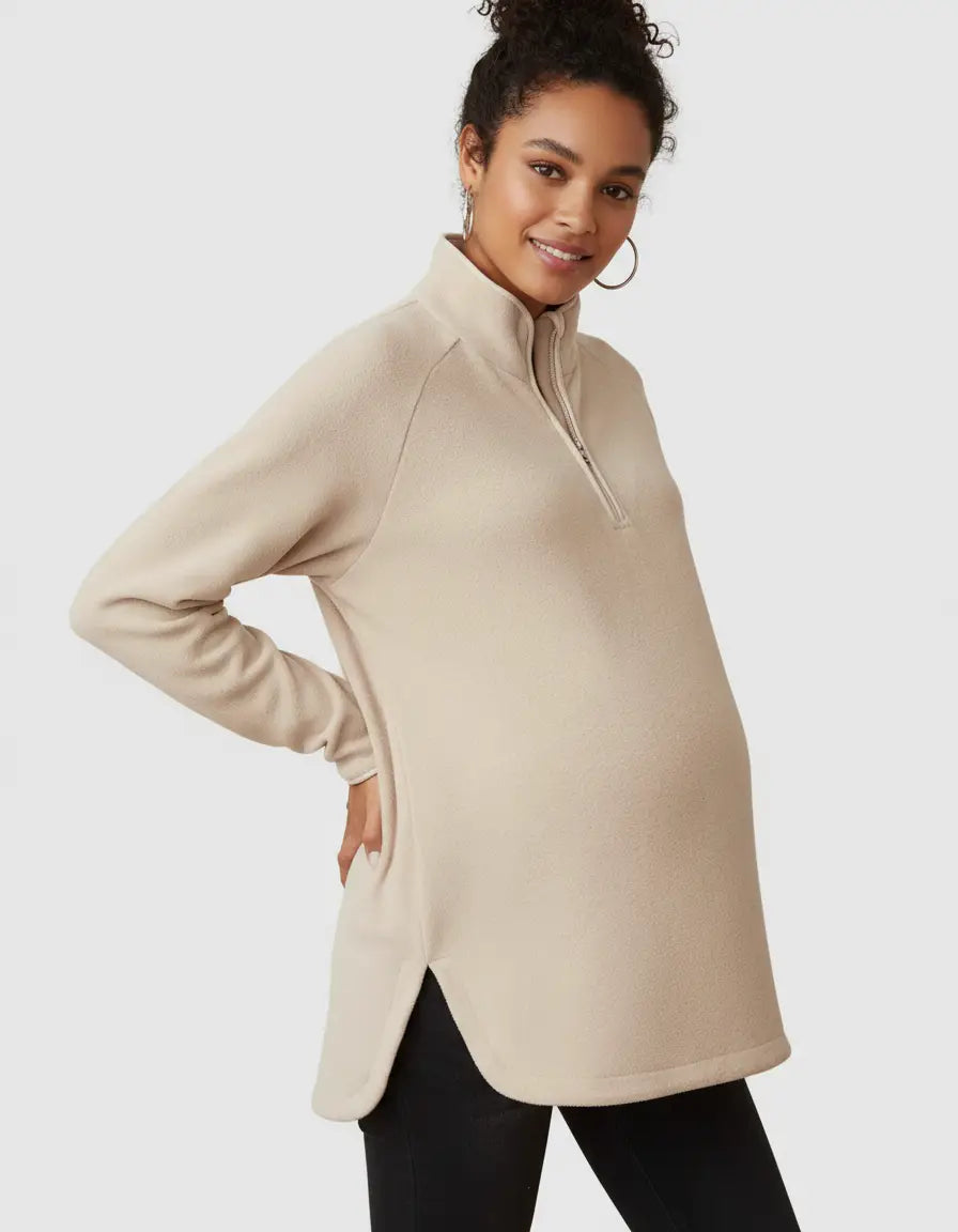 Maternity model wearing a beige soft knit half-zip long sleeve top with side slits.