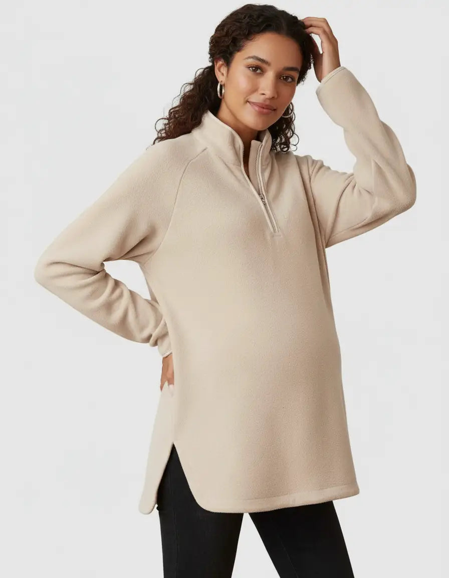 Pregnant woman in a beige soft knit half-zip maternity top with a stand collar and side slits.