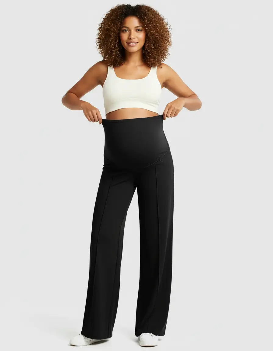 Smiling pregnant woman in a white crop top and black high-waist maternity pants with a relaxed fit.