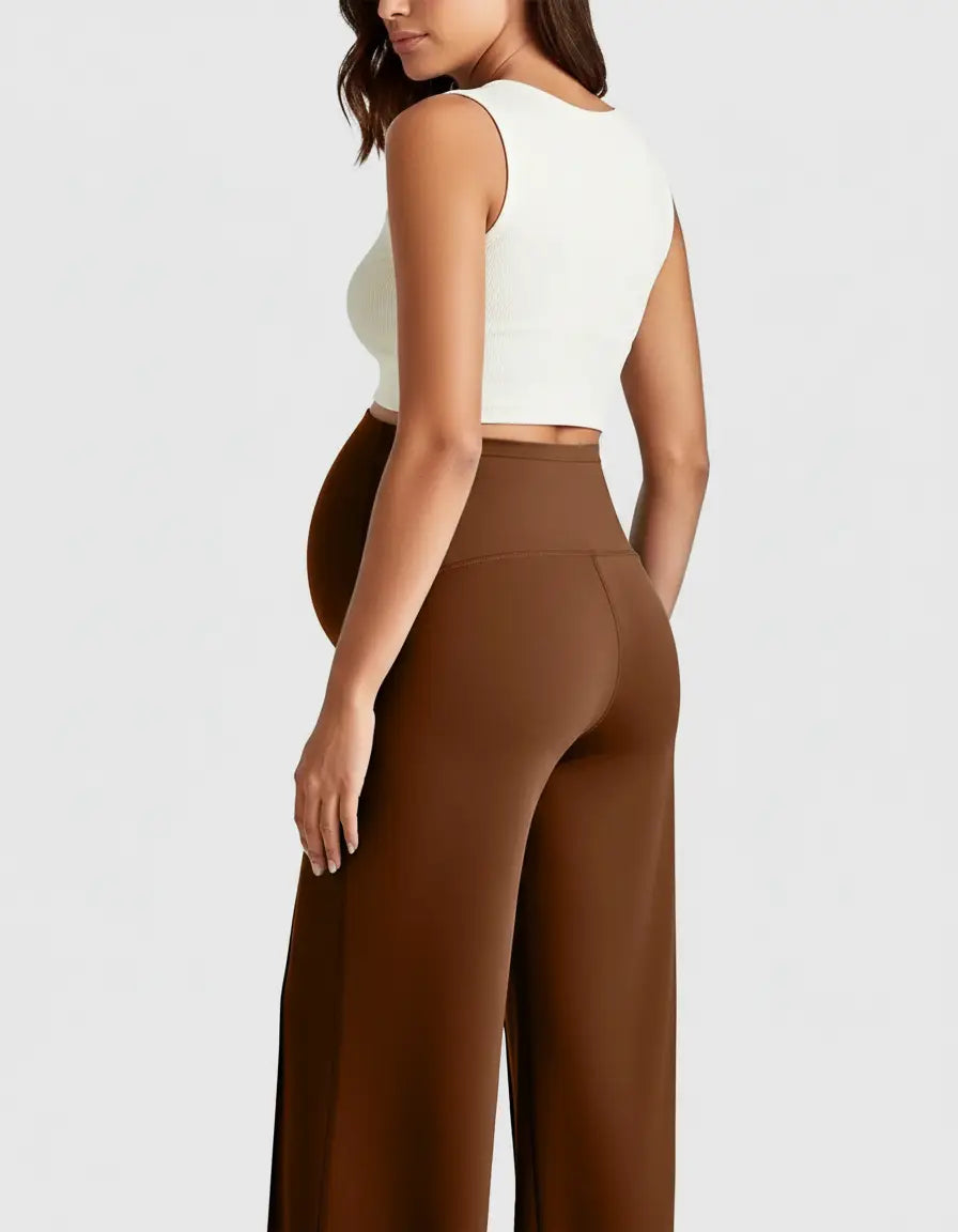Maternity model in brown high-waist, relaxed-fit pants and a white crop top, showing a pregnant belly.